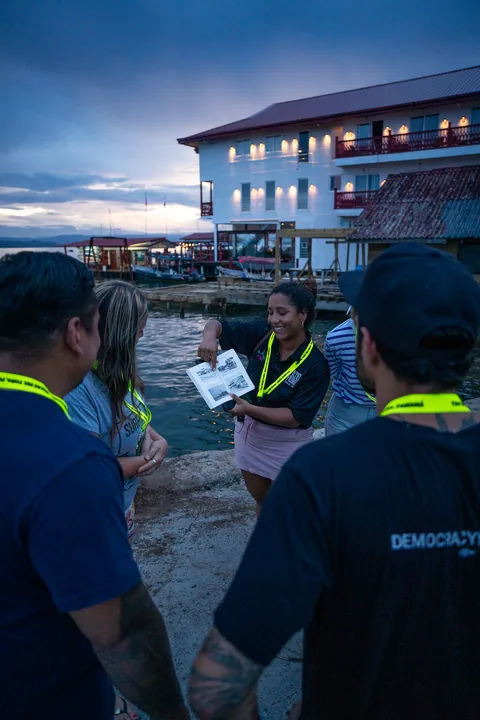 A guide showing an old photo to the group by the water at dusk